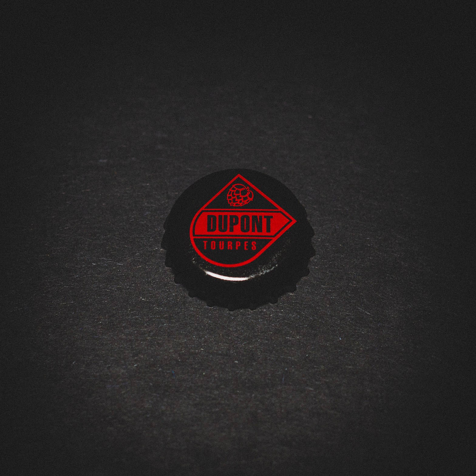 Bottle cap from Brasserie Dupont, set against a high-contrast black backdrop